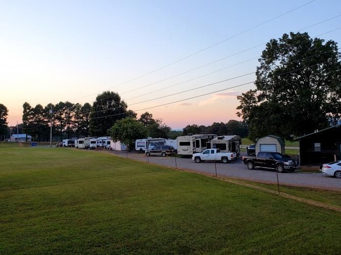 RVs and trailers parked along a grassy roadside at dusk under a pink-blue sky