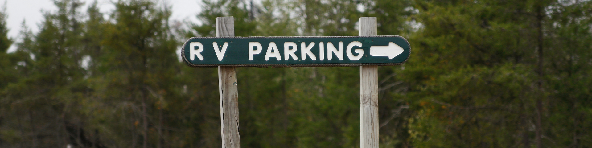Green RV PARKING sign with a right arrow in a wooded area
