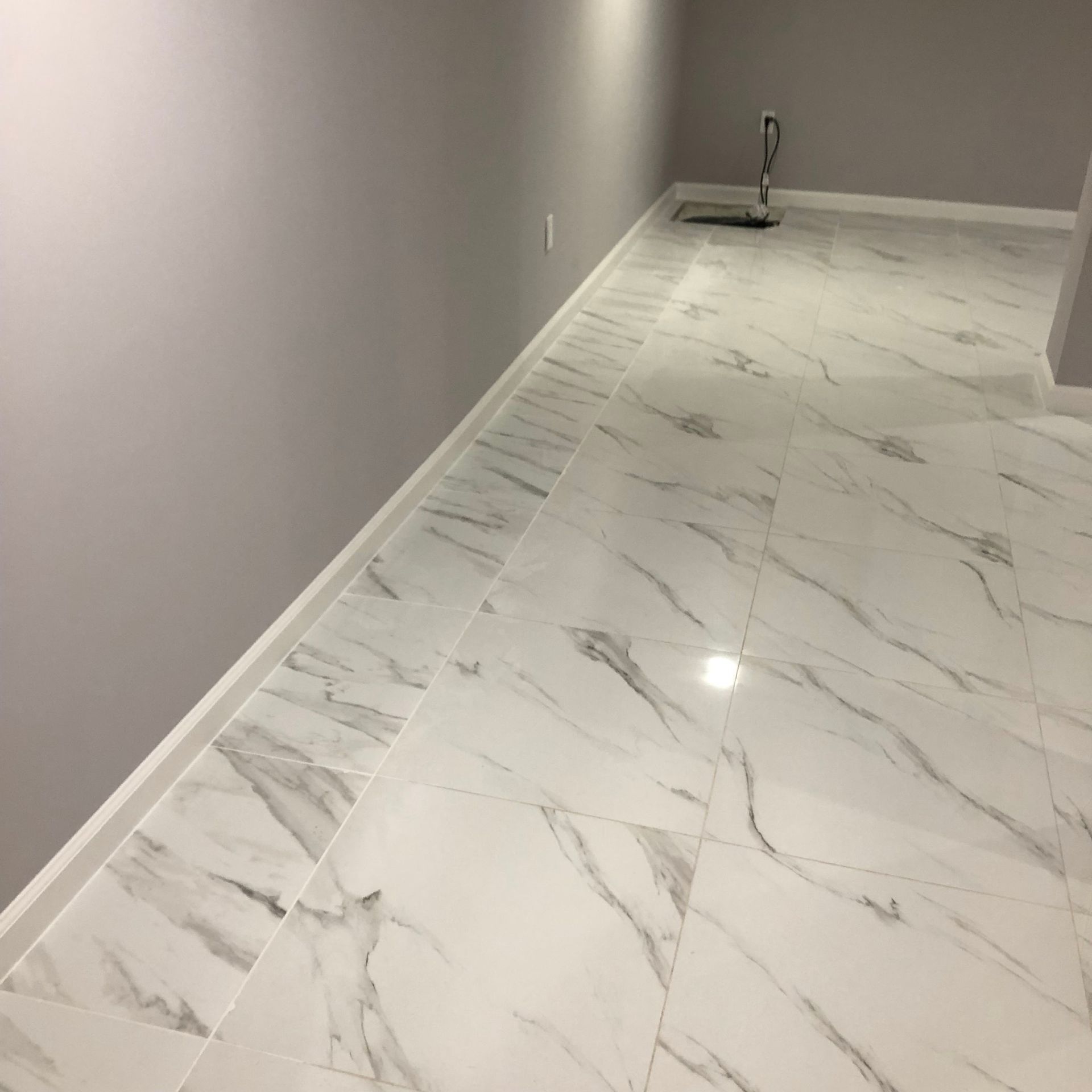 A white tile floor in a room with a gray wall.