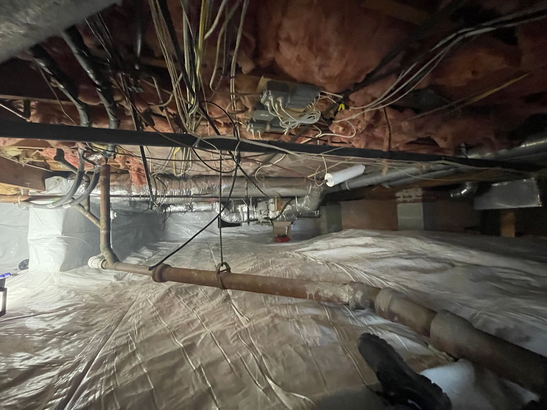 A basement with a lot of pipes and wires hanging from the ceiling.