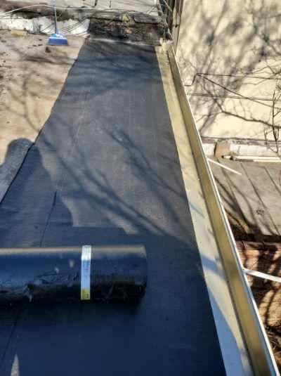 A roll of roofing material is sitting on top of a roof next to a gutter.