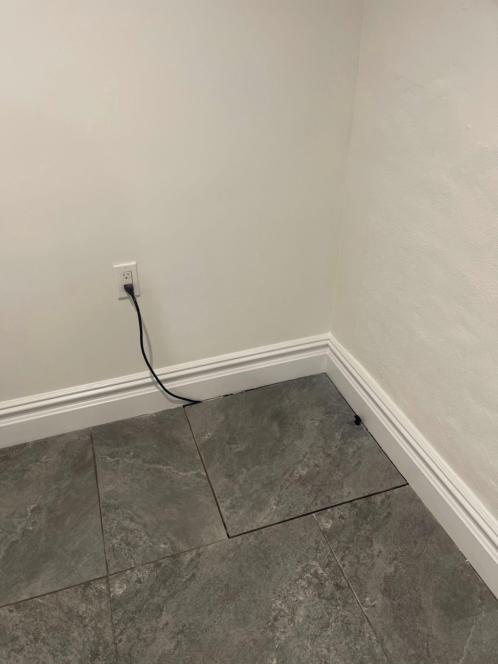 A corner of a room with a tile floor and a power cord coming out of the wall.