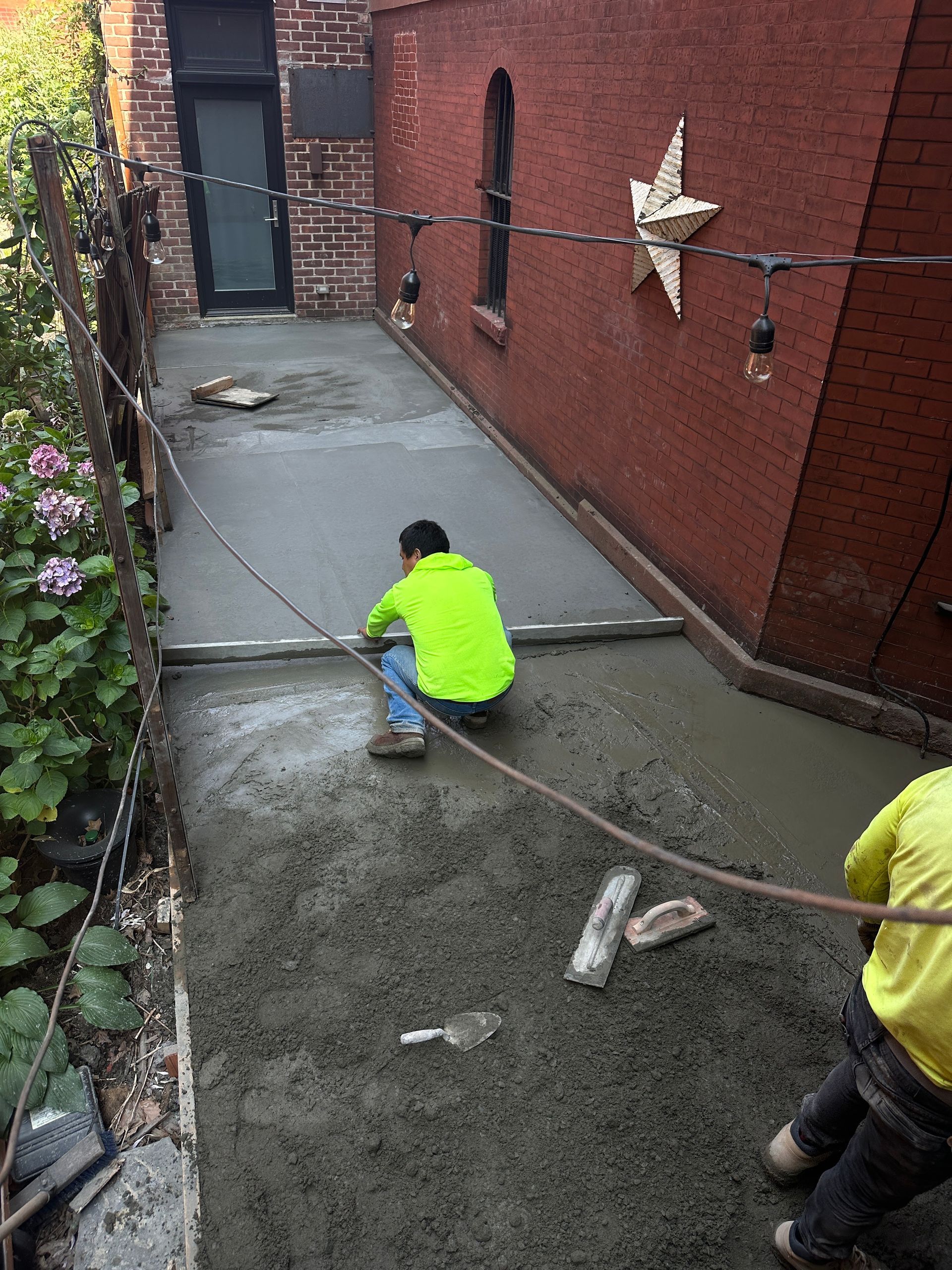 A man in a neon yellow jacket is kneeling on a concrete sidewalk.