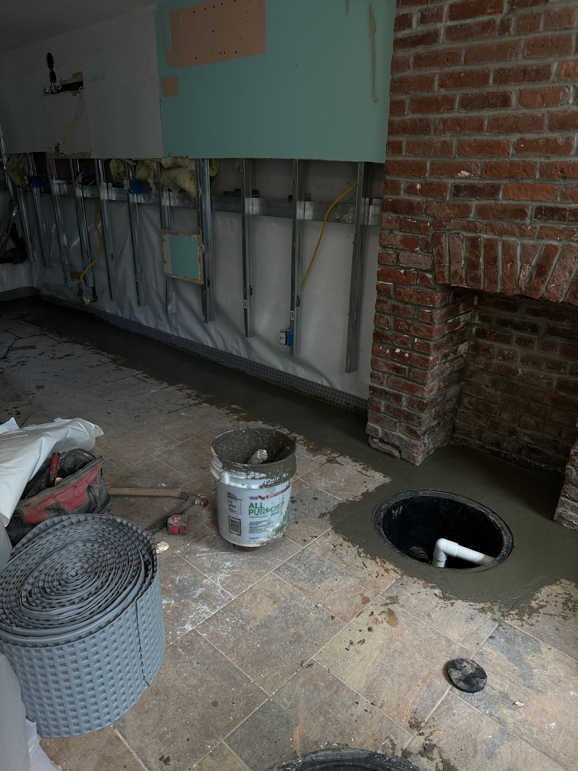 A bucket of concrete is sitting on the floor next to a brick wall.