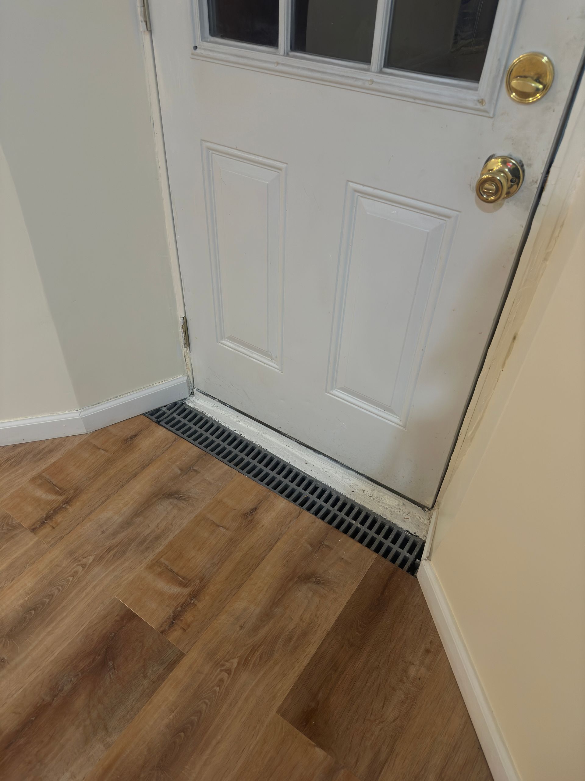 A white door with a drain underneath it in a hallway.