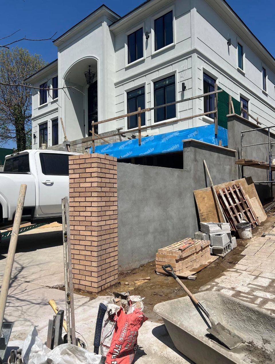 A white truck is parked in front of a white house under construction.