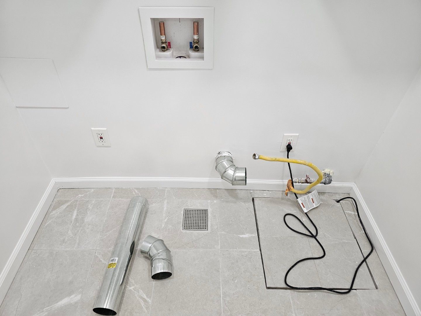 A laundry room with a drain and pipes on the floor.