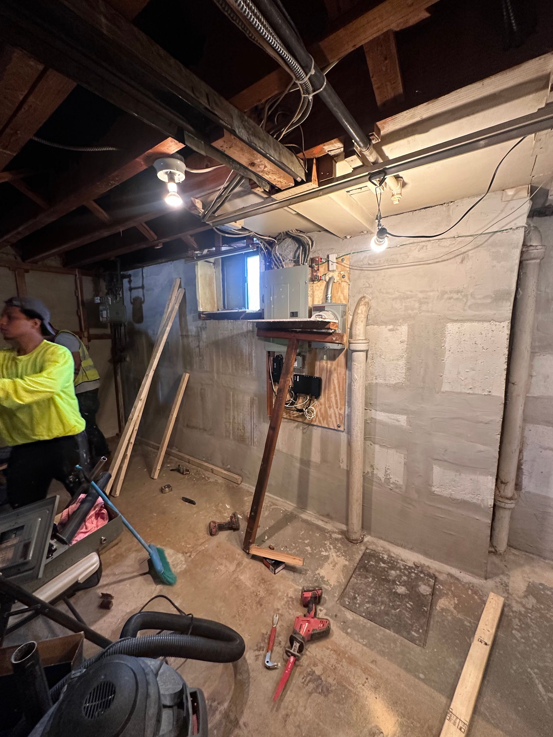 A man is working in a basement with tools and a vacuum cleaner.