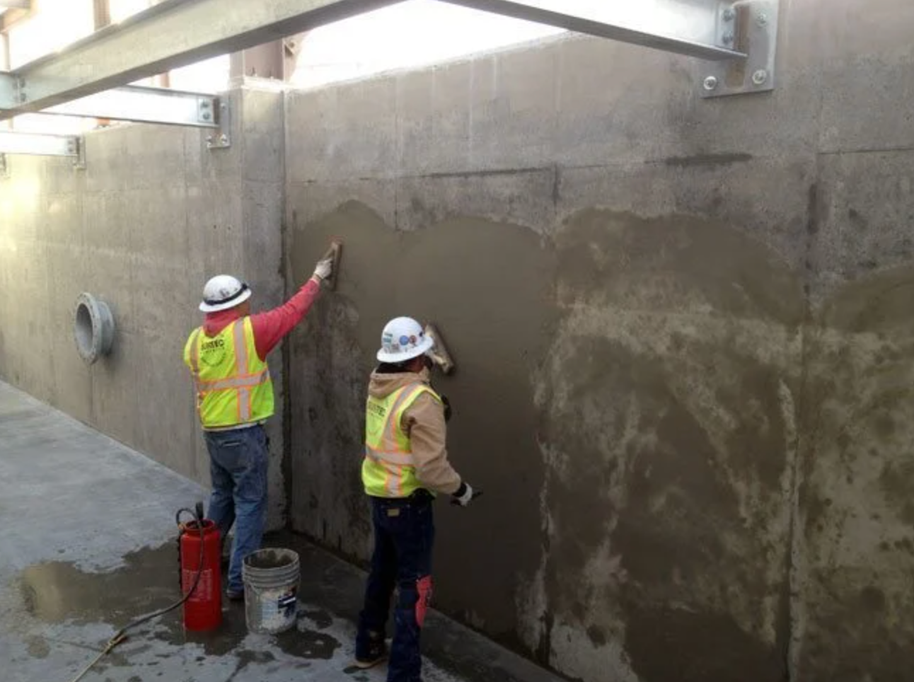 Two workers applying stucco to a concrete wall in an outdoor setting.