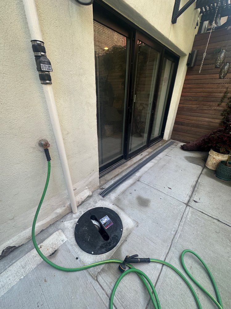 A green hose is connected to a drain on the side of a building.