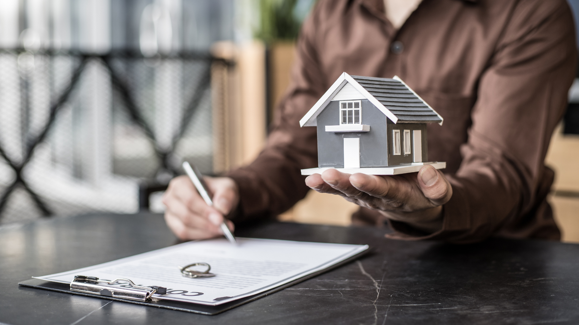 A man is holding a model house and writing on a clipboard.
