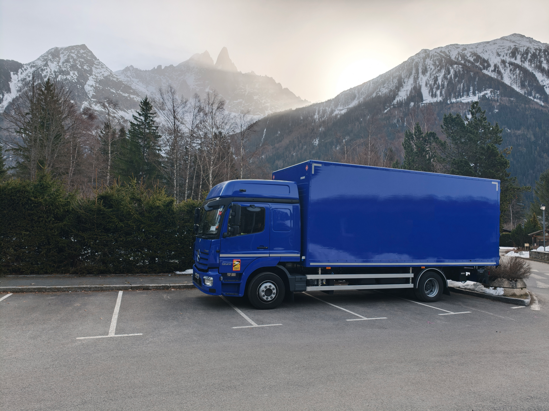 Blue Class 1 truck parked in a mountain lot with snowy peaks in the background.