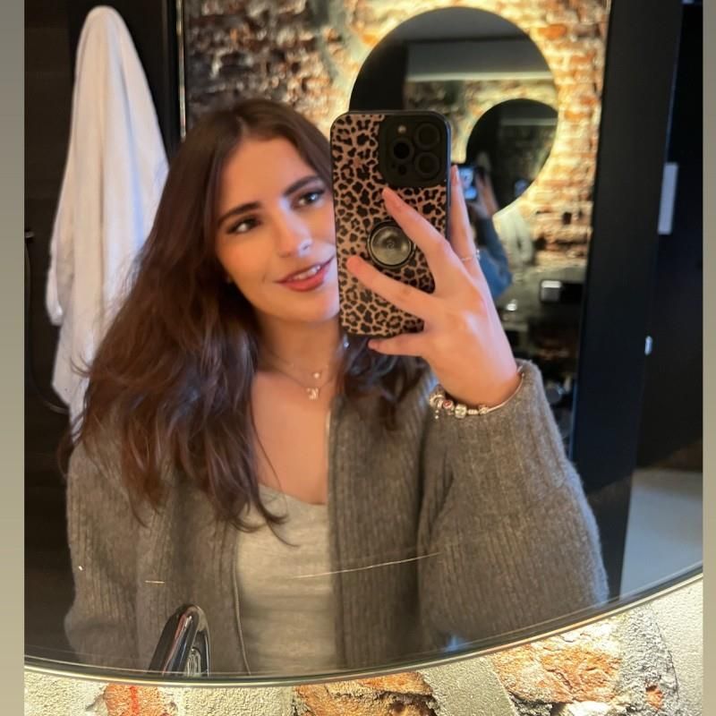 Woman taking a mirror selfie in a bathroom; she's wearing a gray sweater and holding a leopard print phone case.