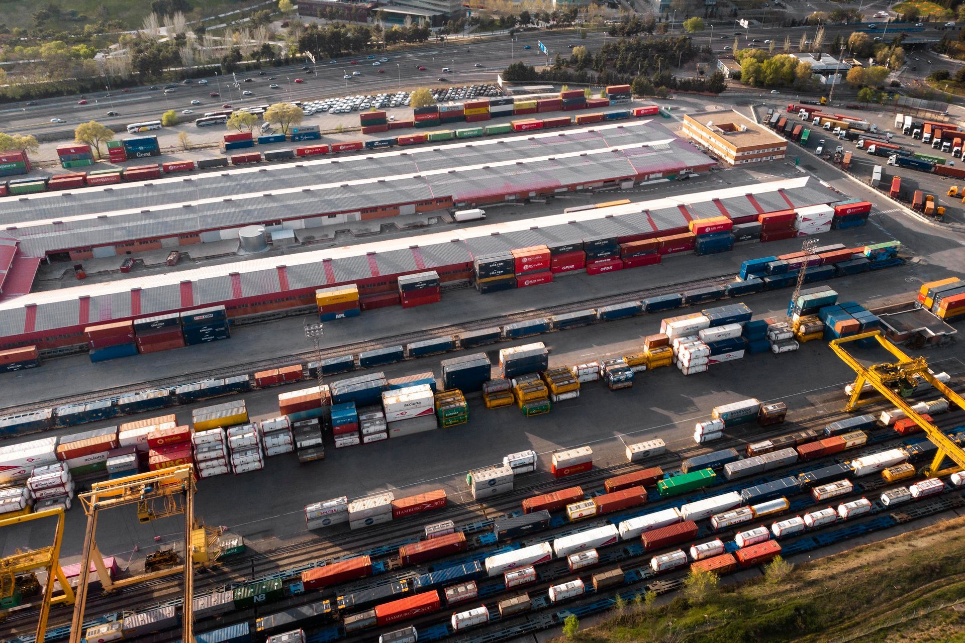 Aerial view of a busy rail yard with rows of freight trains, shipping containers, and cranes