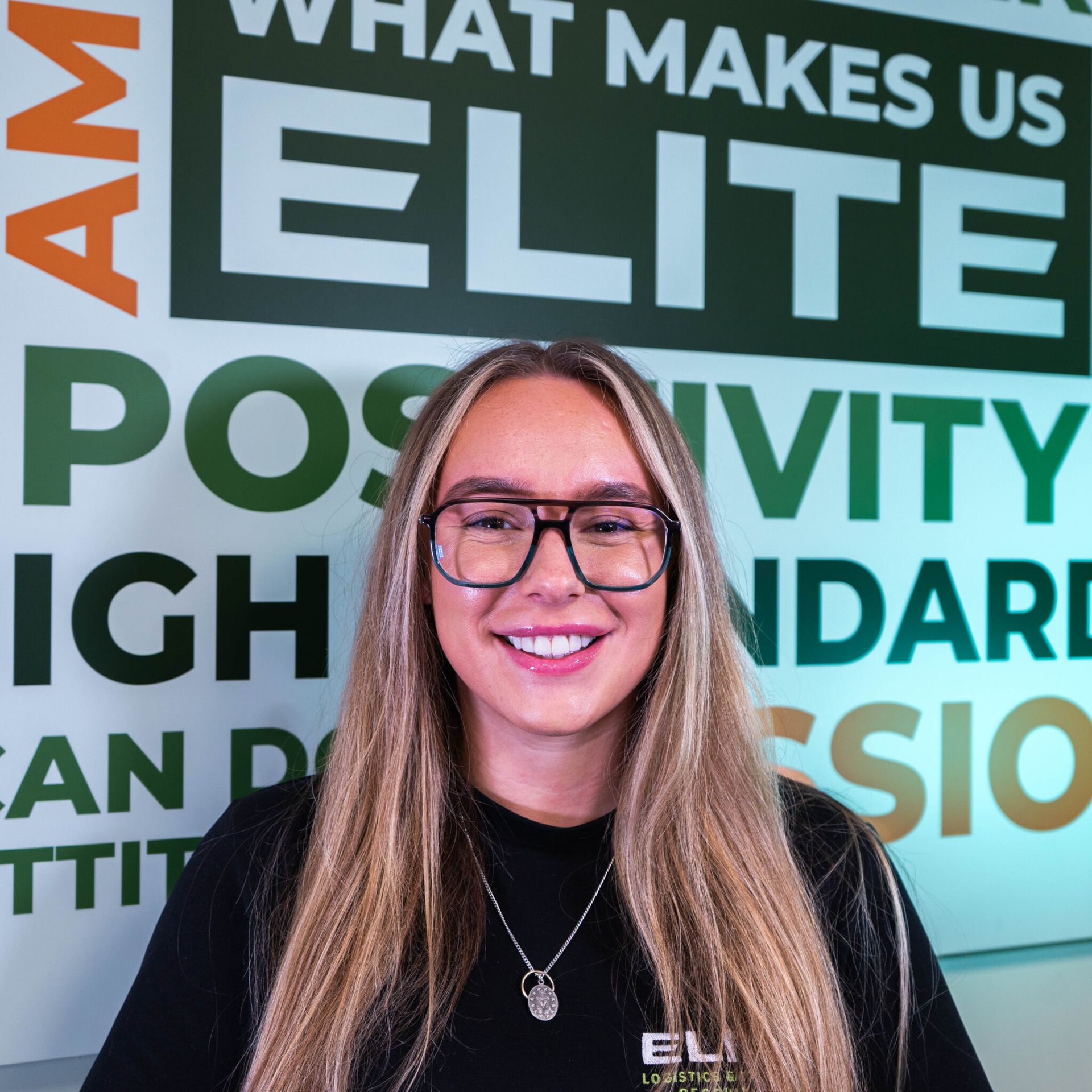 Woman with glasses smiles in front of a wall with