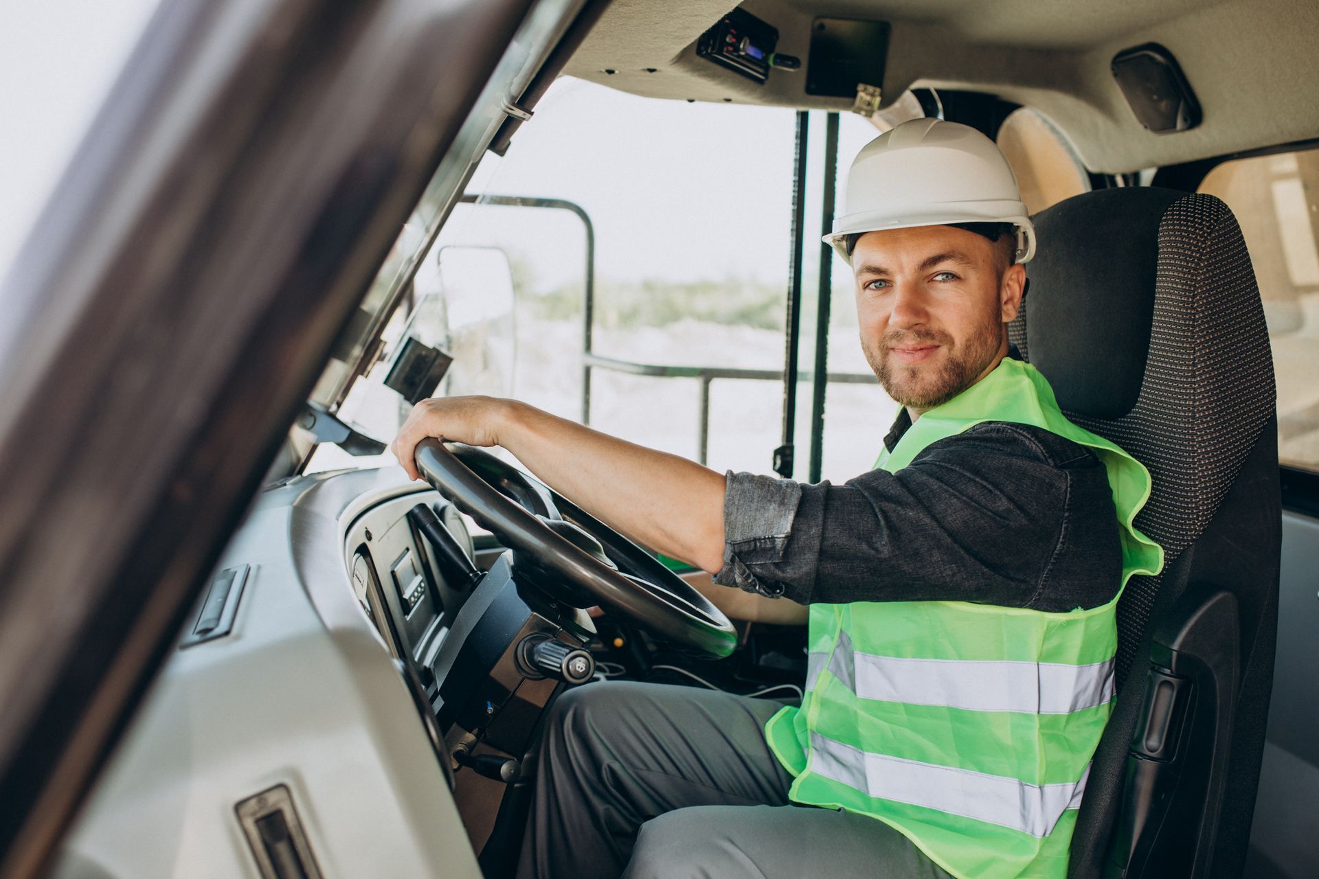 Man in hard hat and safety vest, driving a large vehicle, smiling.
