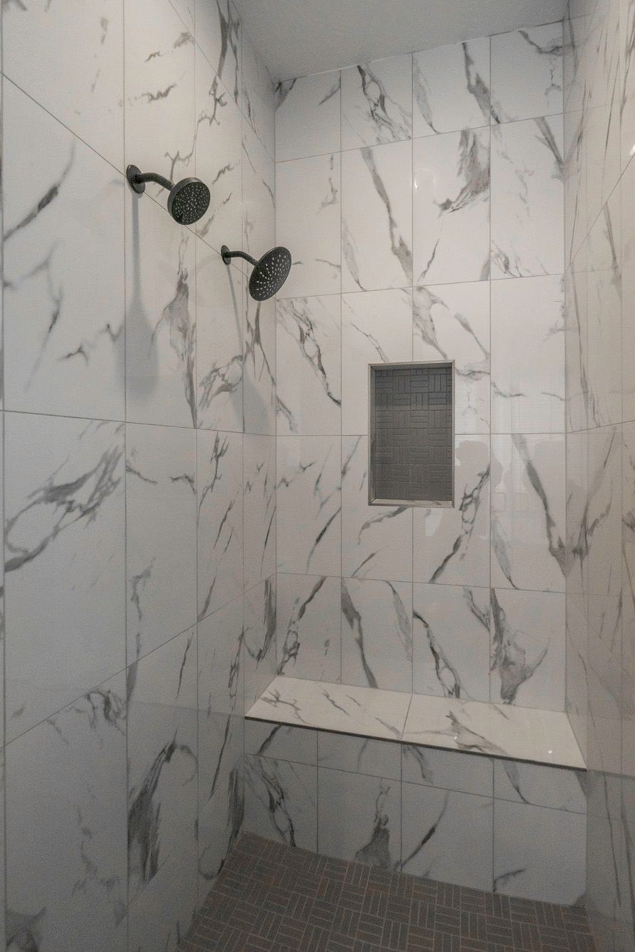 A walk in shower with marble tiles and a bench.