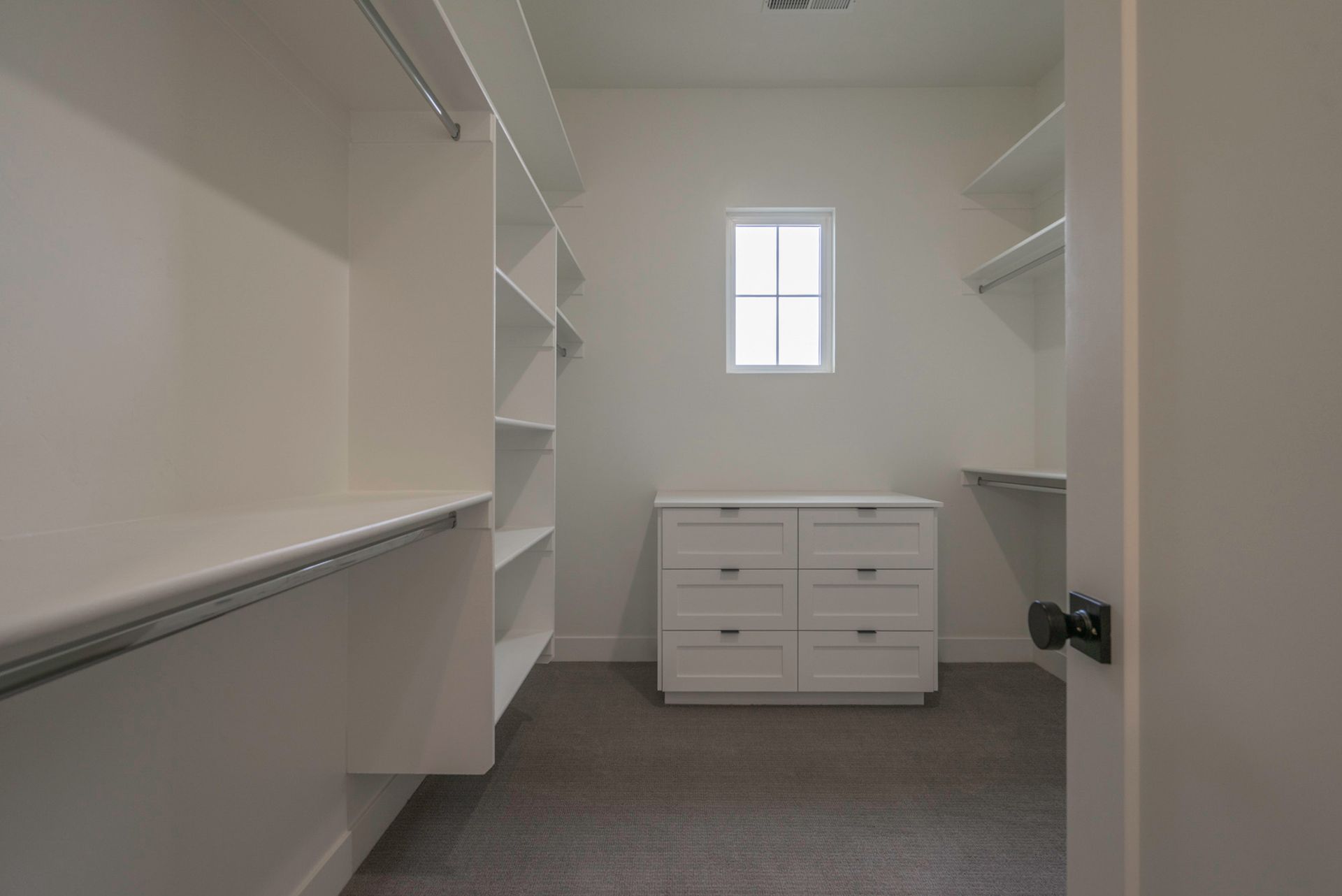 A walk in closet with lots of shelves and drawers and a window.