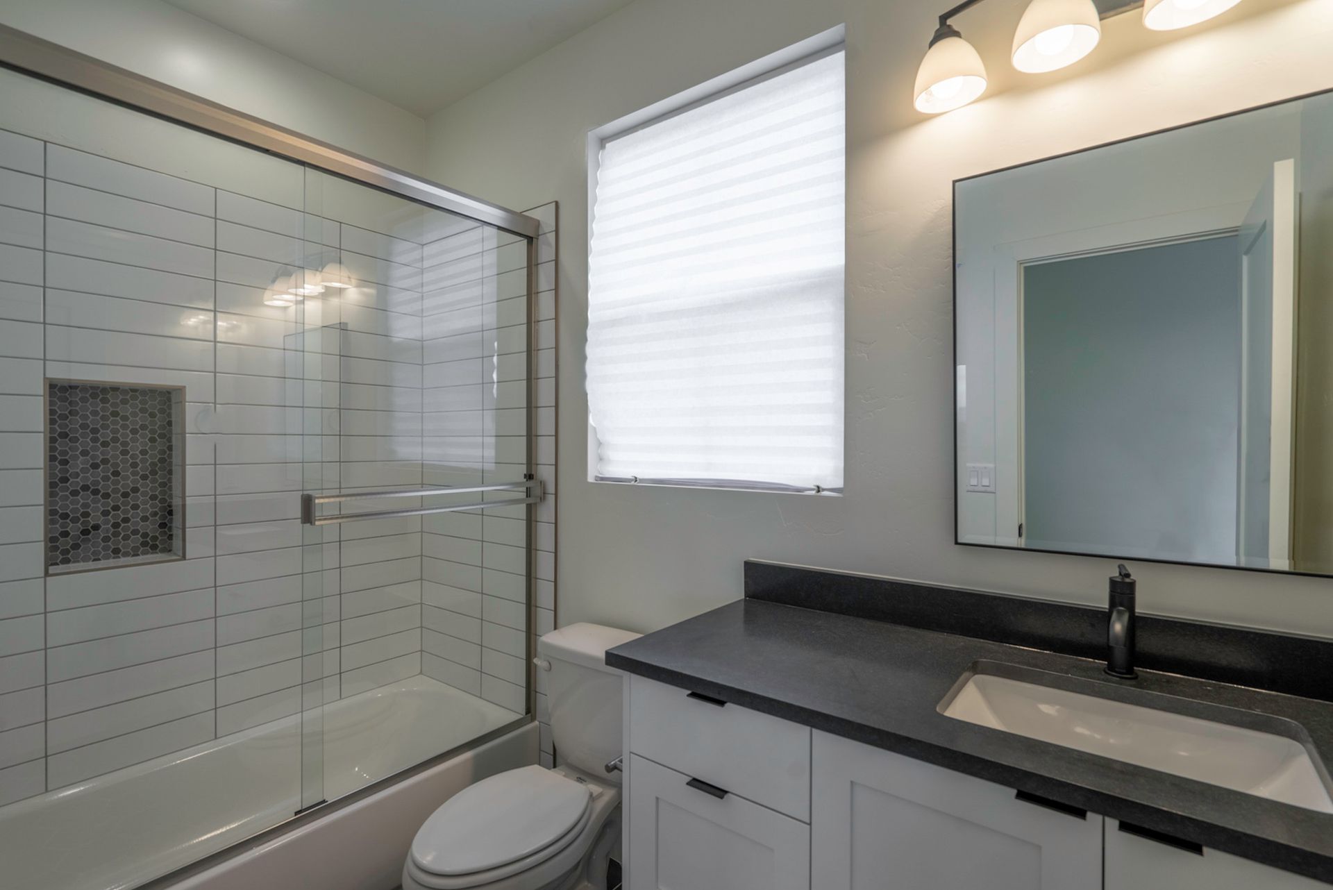 A bathroom with a toilet , sink , shower and window.