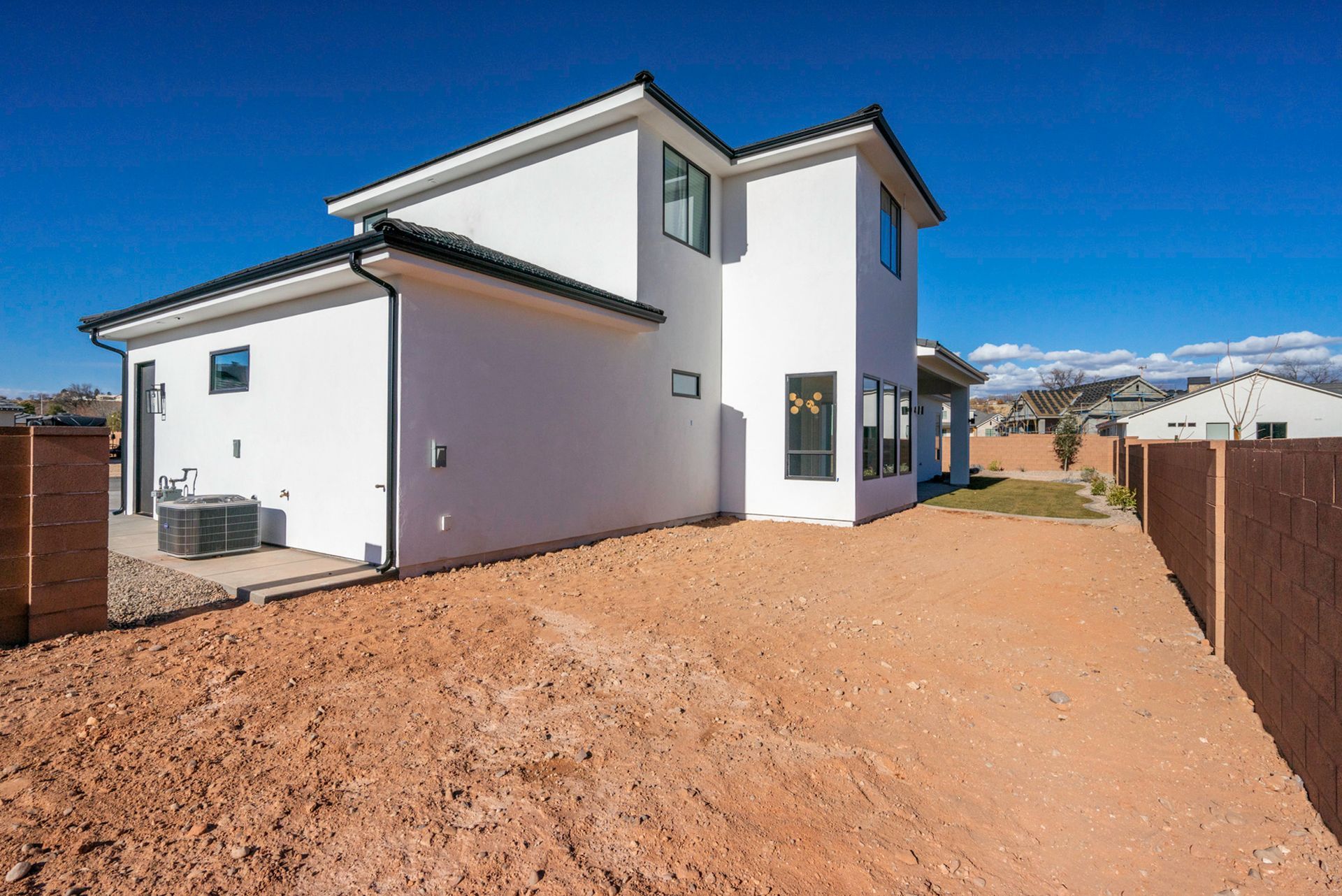 A white house is sitting on top of a dirt hill next to a fence.