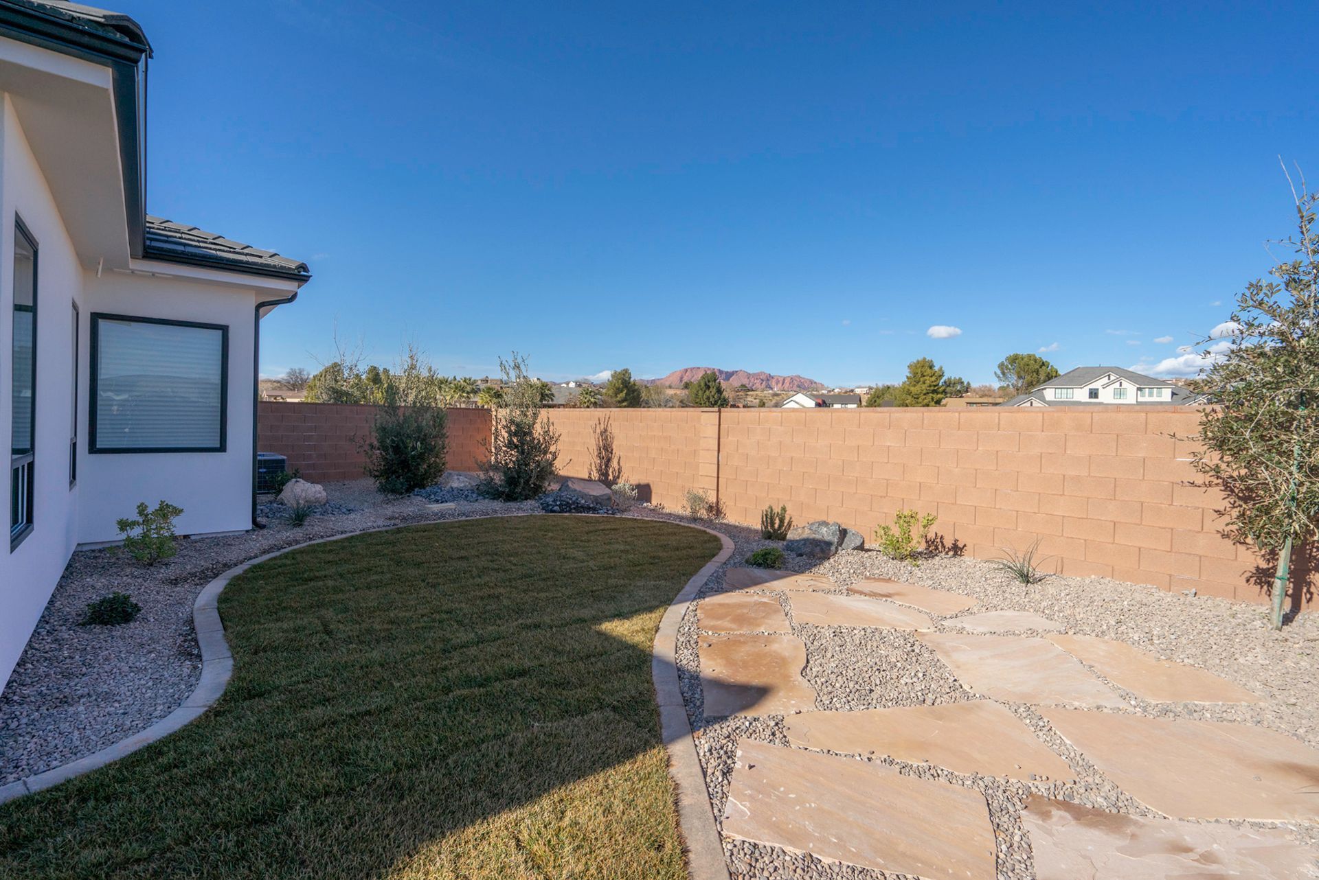 The backyard of a house with a large lawn and a brick wall.