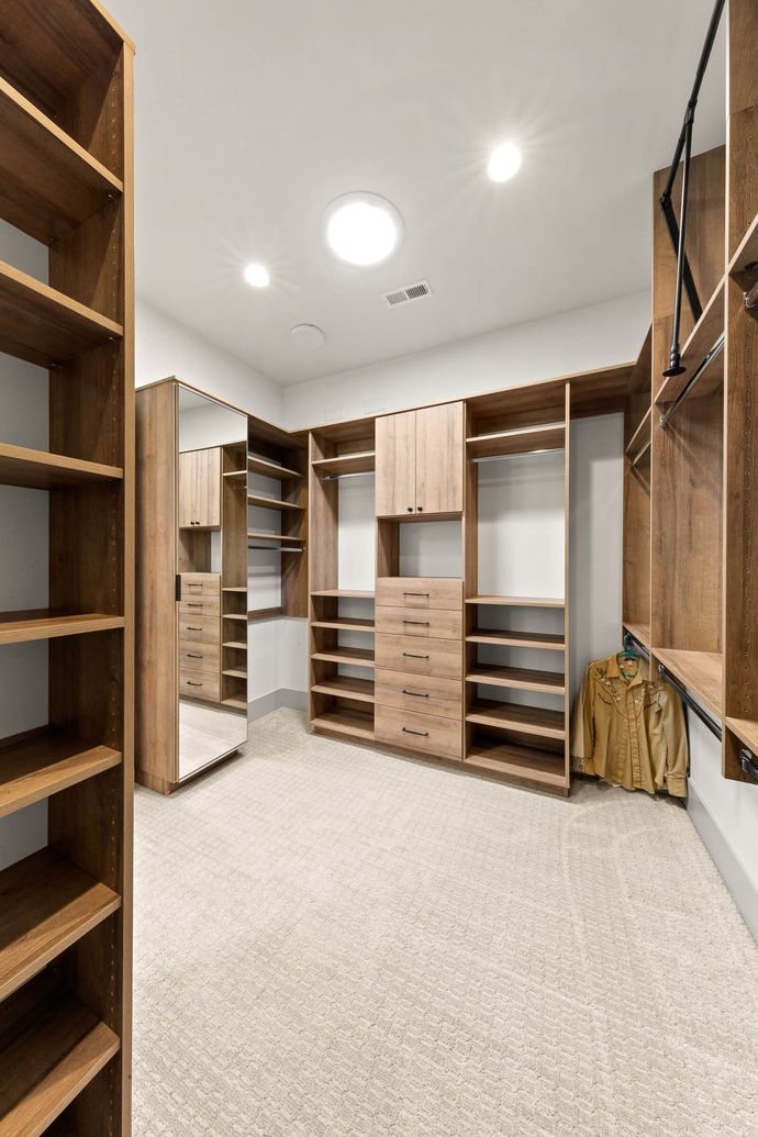 A walk in closet with wooden shelves , drawers , and a mirror.