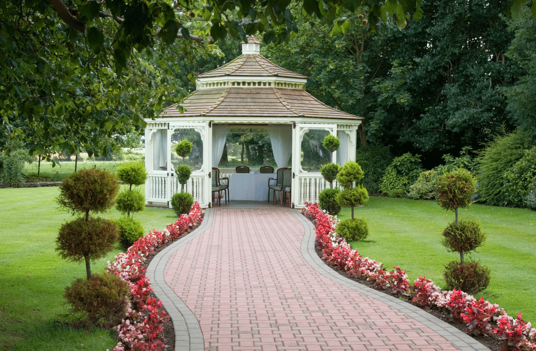 A white gazebo with a brick walkway leading to it