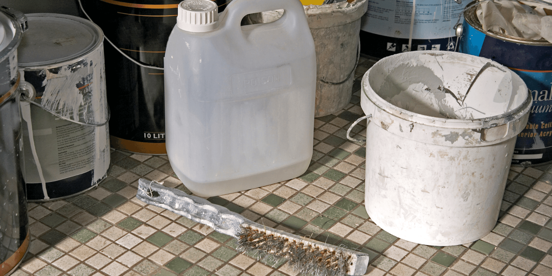 A bunch of buckets of paint are sitting on a tiled floor.