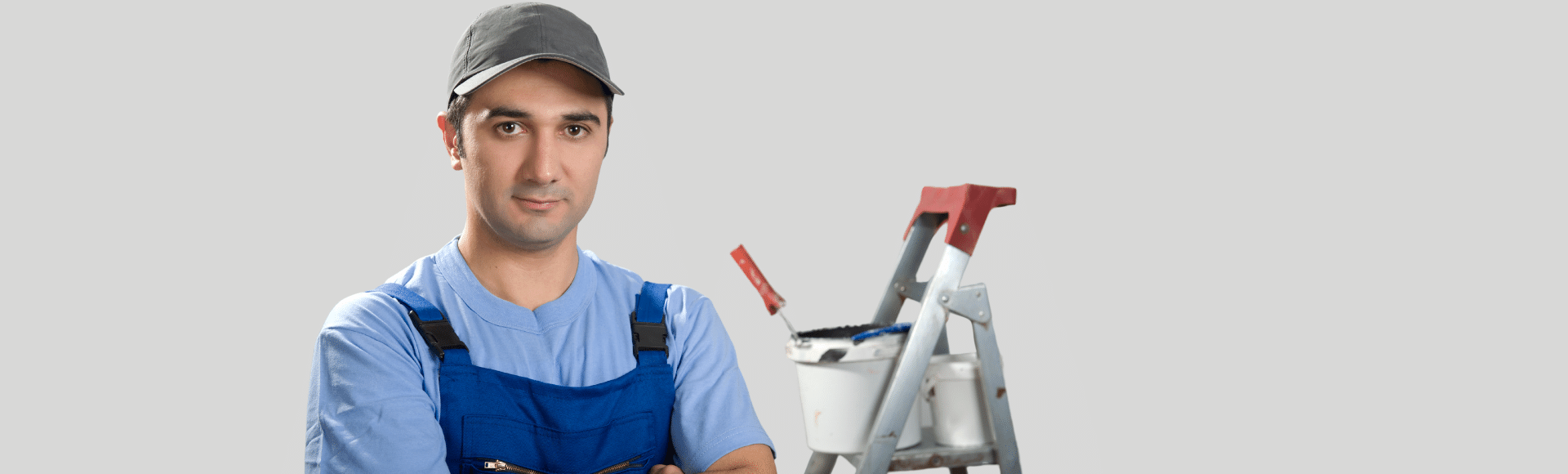 A man in blue overalls is standing next to a ladder.