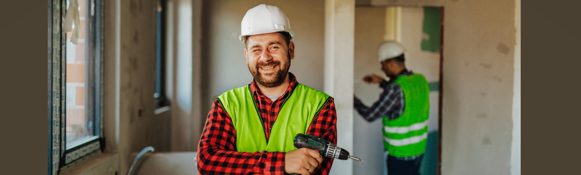 A construction worker is smiling while holding a drill in a room.