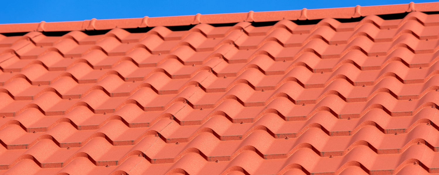 A close up of a red tiled roof with a blue sky in the background.