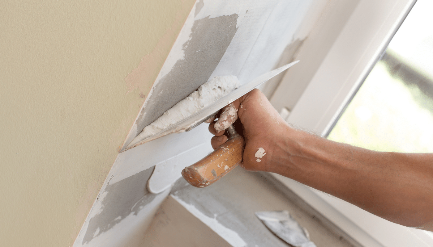 A person is plastering a wall with a trowel.