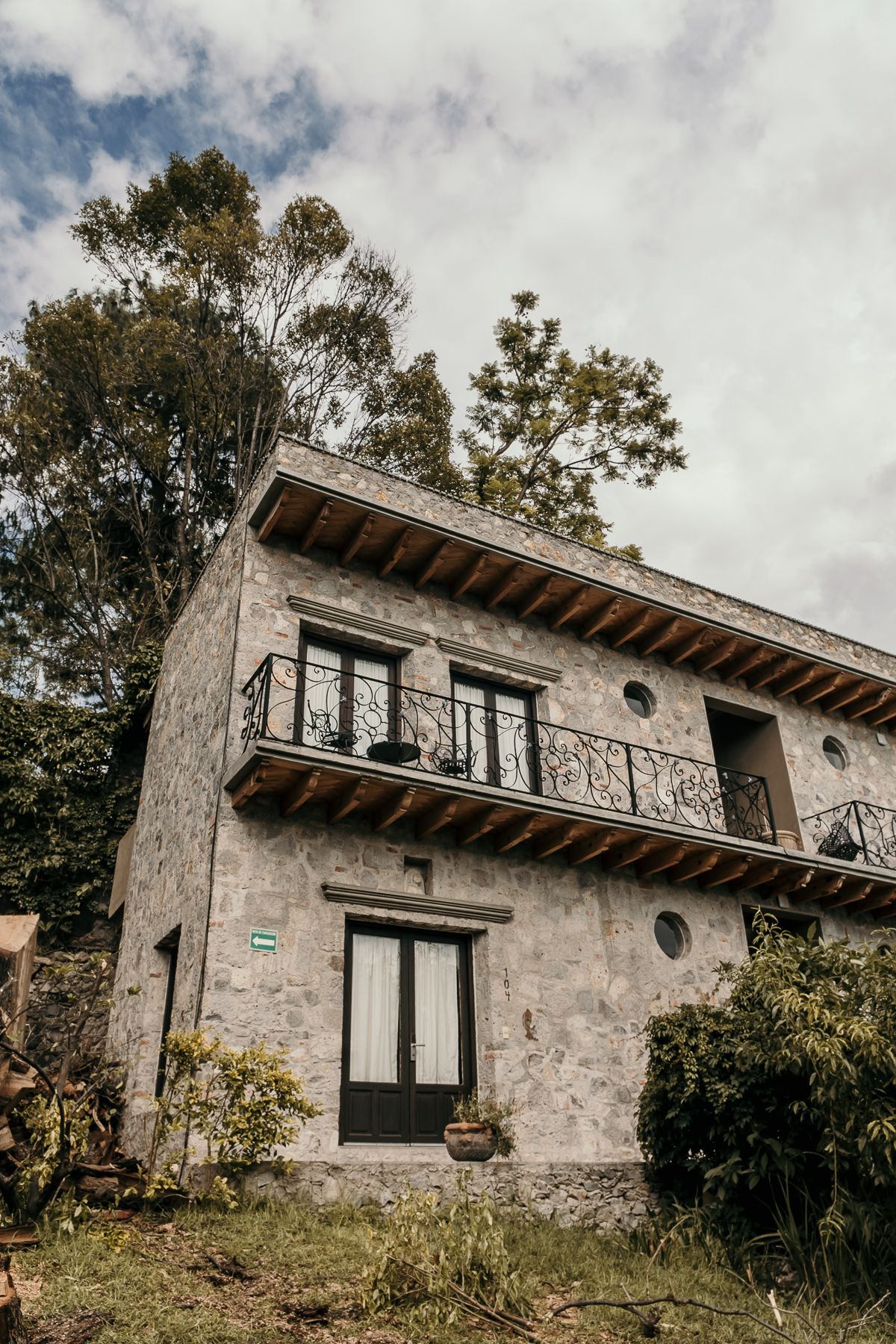 Edificio de piedra con balcón, árboles y cielo nublado.