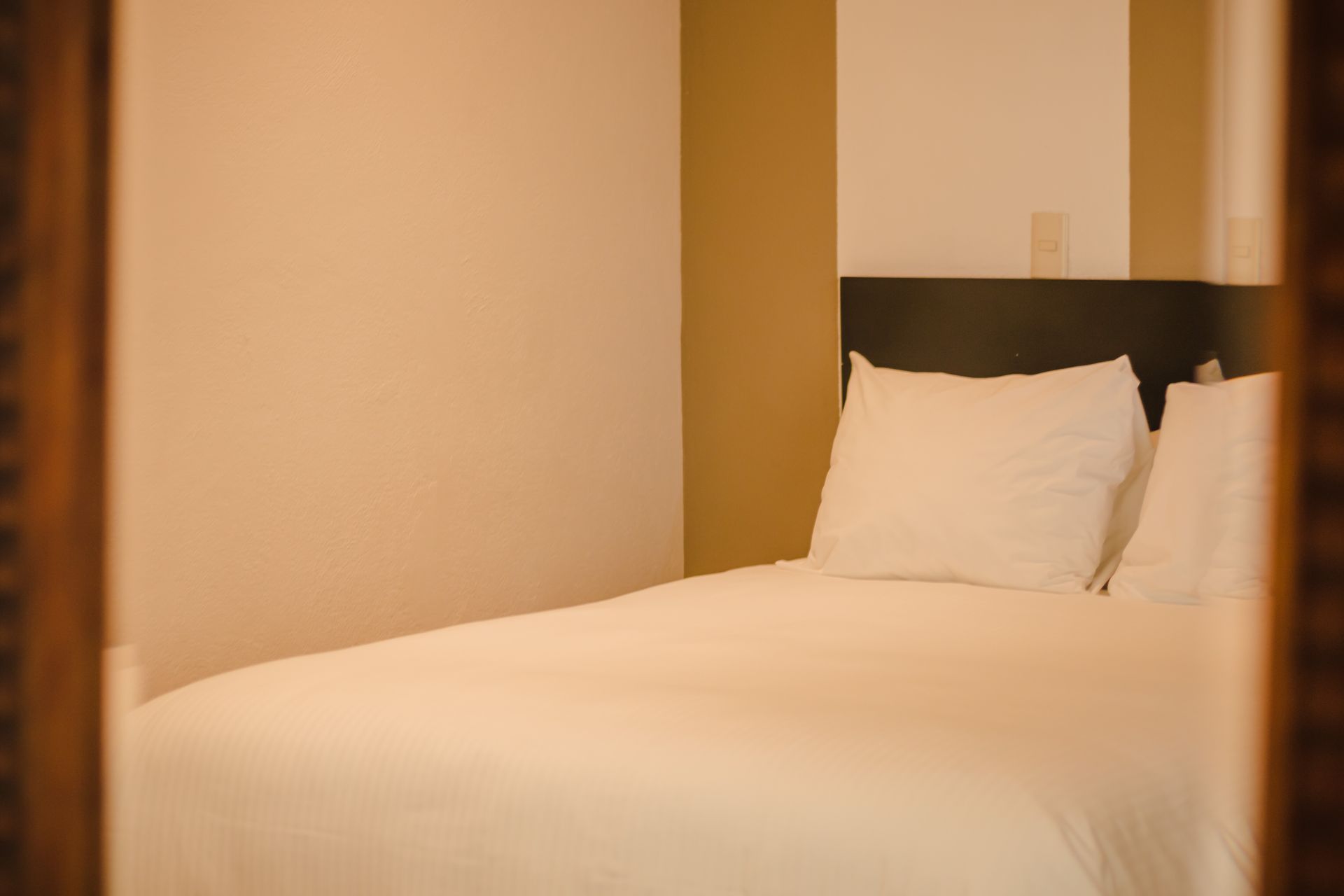 Cama con ropa de cama y almohadas blancas, vista a través de un marco de madera.