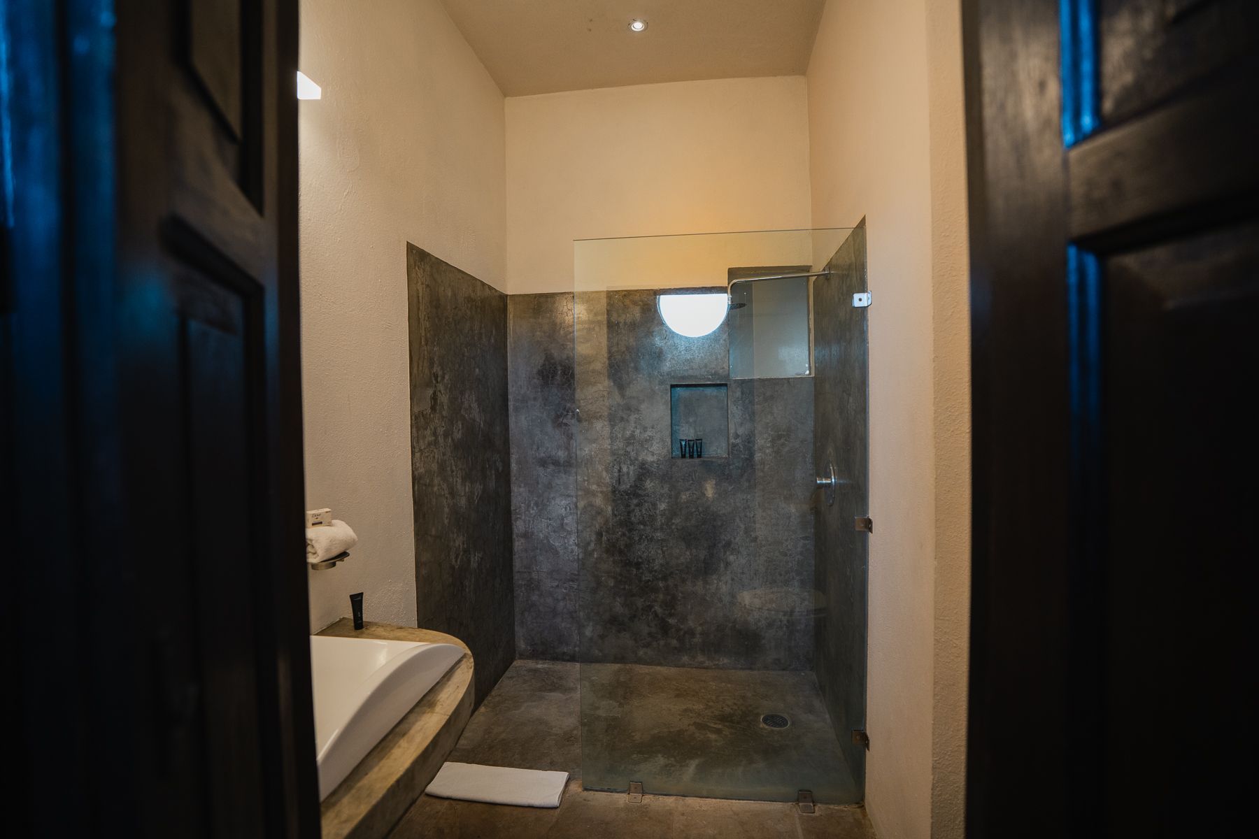 Baño con ducha, paredes de hormigón, bañera blanca y puerta abierta.