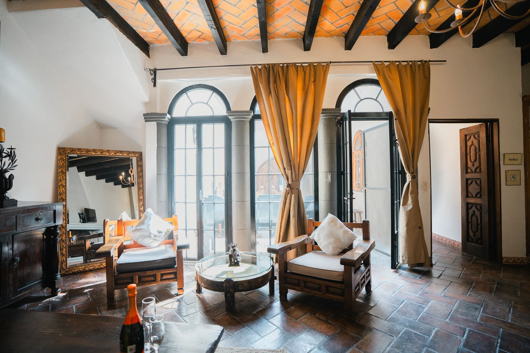 Amplia habitación con puertas abiertas y ventanas arqueadas, dos sillones de madera y una mesa redonda.