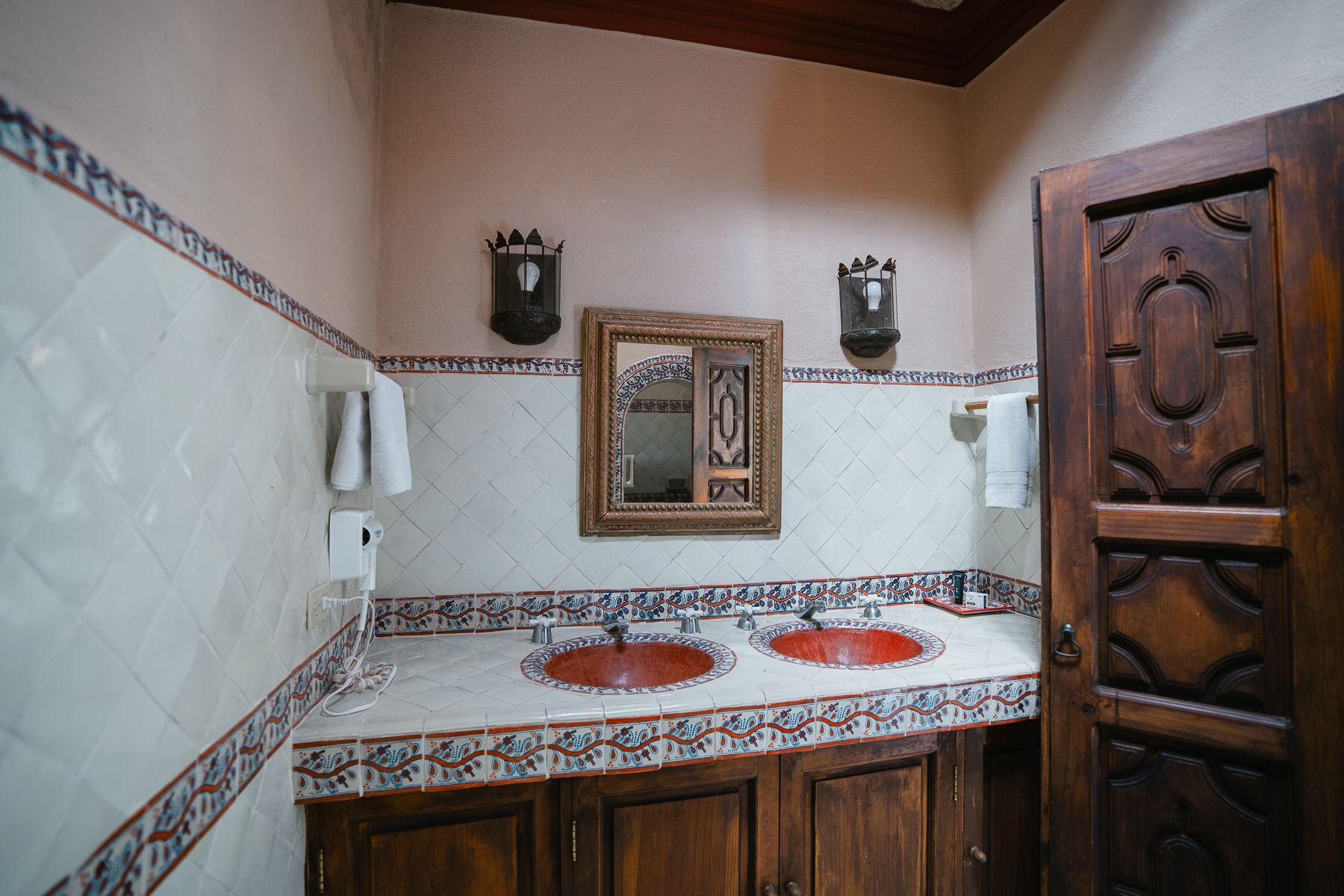 Baño con muebles de madera marrón, dos lavabos rojos, espejo y paredes revestidas con molduras decorativas.