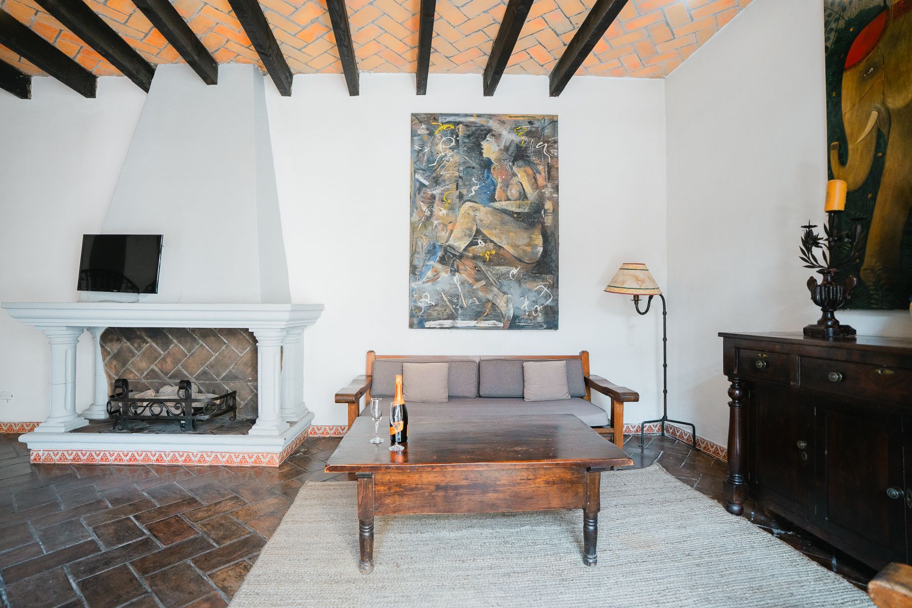 Sala de estar con chimenea, sofá, arte y vigas de madera en el techo.