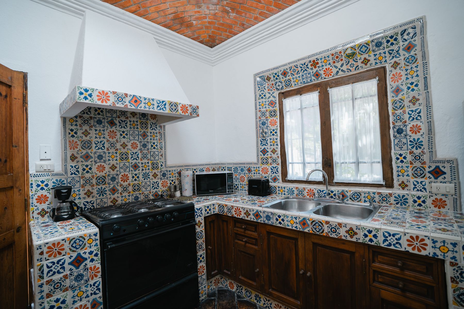 Cocina con salpicadero de azulejos de colores y encimeras, estufa negra, gabinetes de madera y ventana.