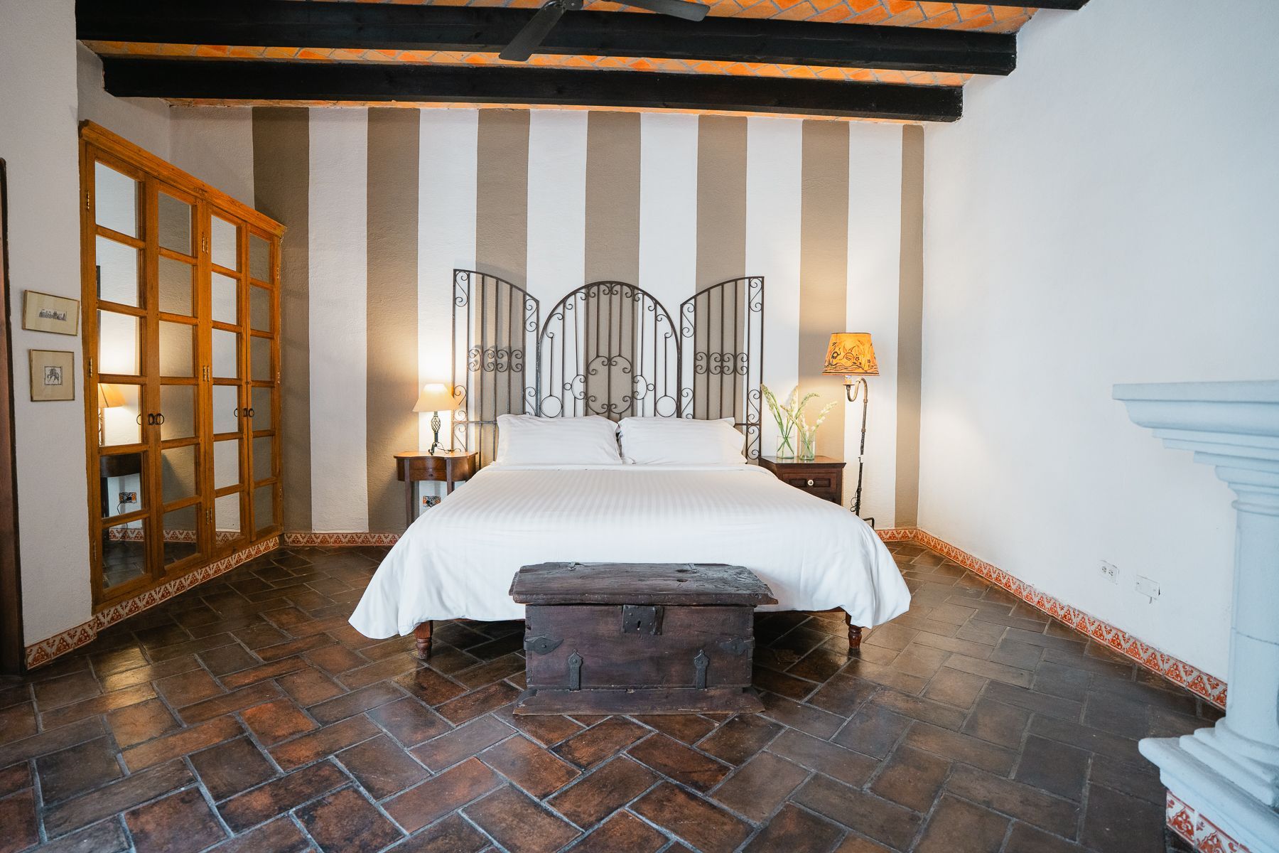 Dormitorio con ropa de cama blanca, paredes rayadas y suelos de madera oscura.