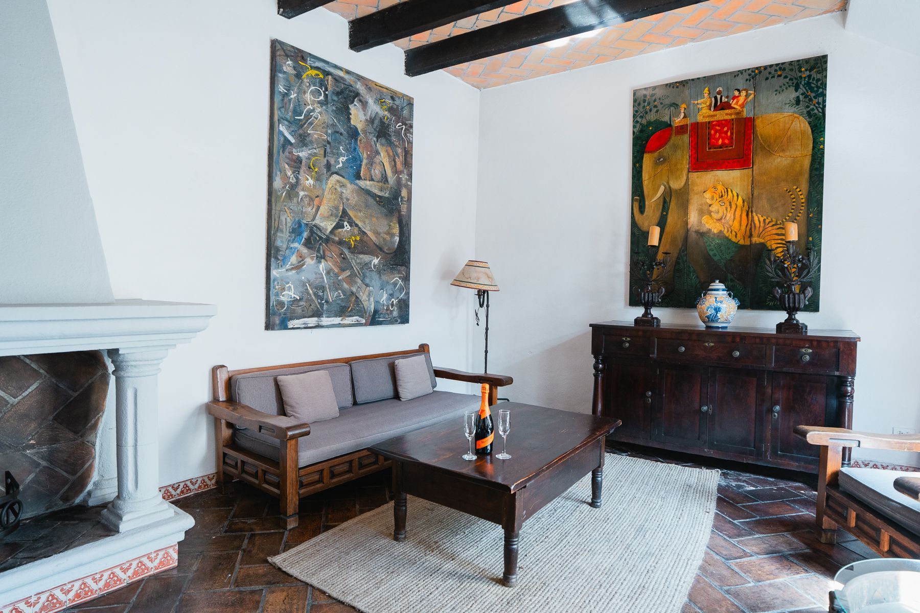 Sala de estar con arte, muebles de madera oscura, paredes blancas y chimenea.