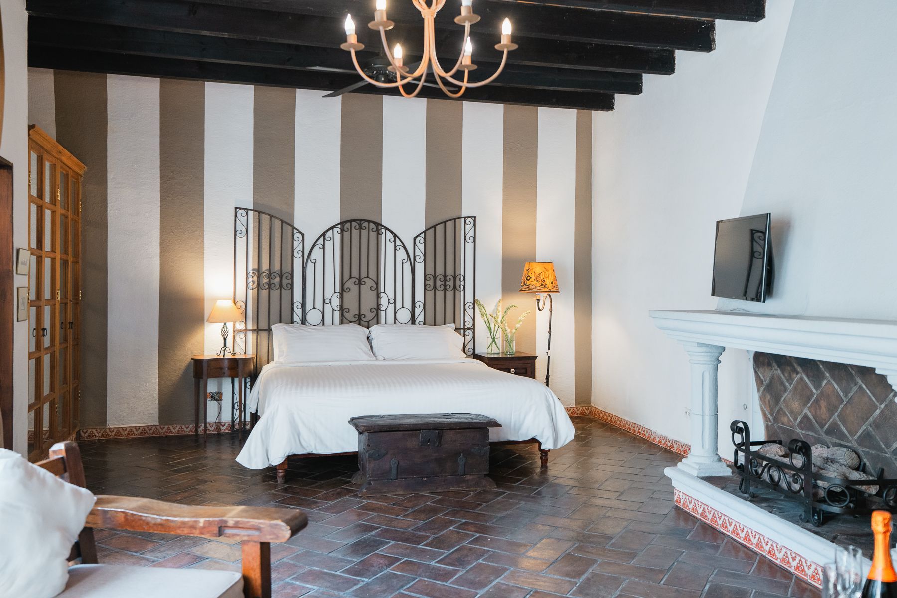 Dormitorio con pared rayada, chimenea, cabecero de hierro forjado y lámpara de araña.