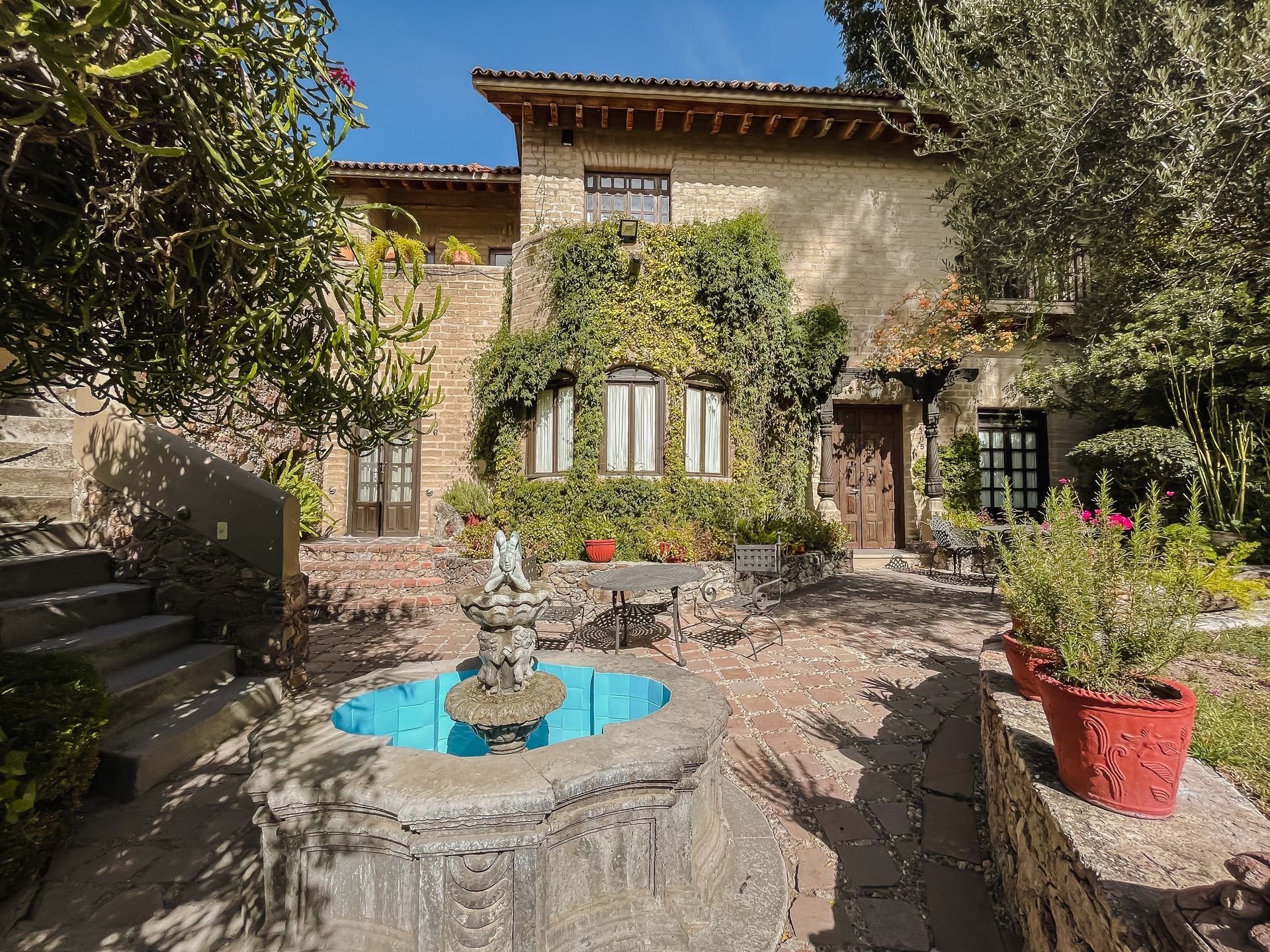 Patio con fuente de piedra y edificio con enredaderas.