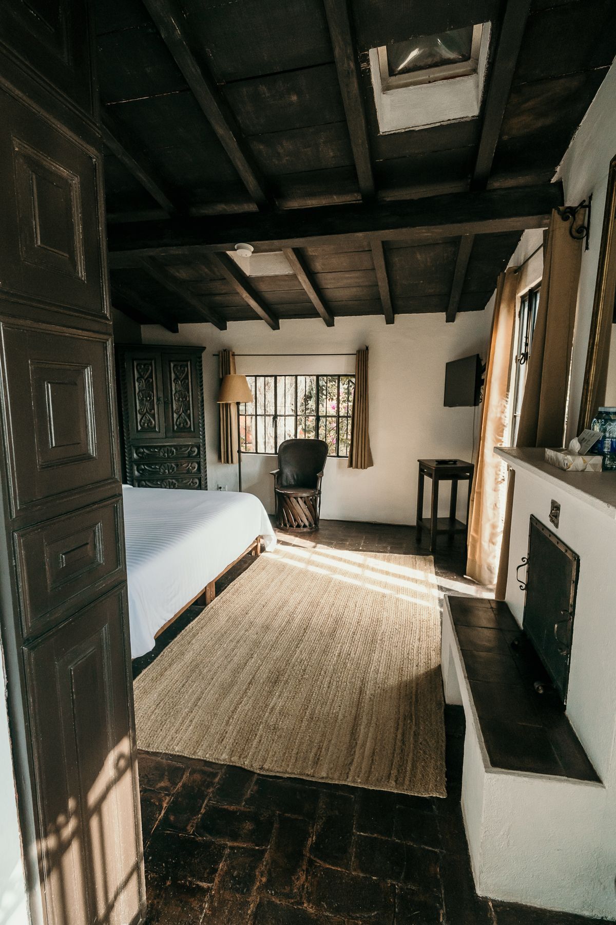 Acogedor dormitorio con vigas de madera a la vista, chimenea y una alfombra grande.