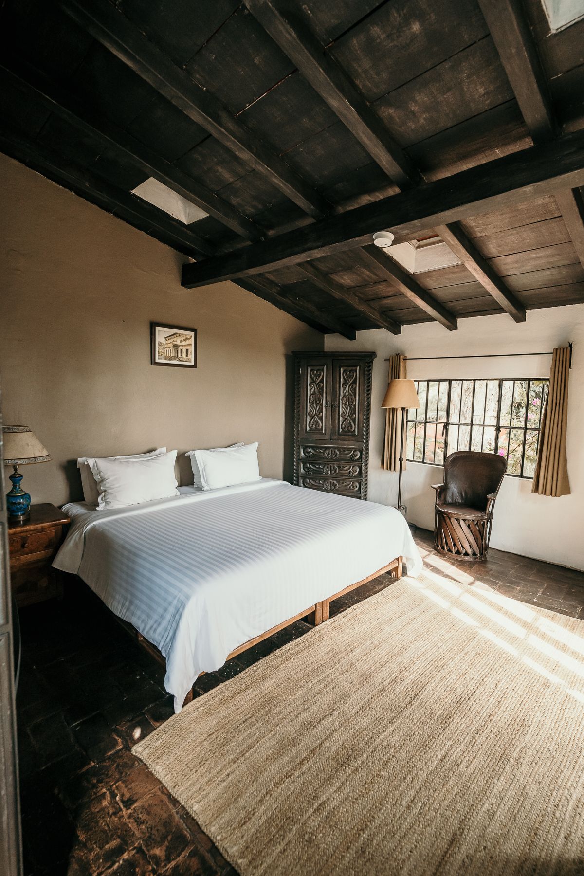 Dormitorio con cama, alfombra, puerta de madera oscura y ventana con luz solar.