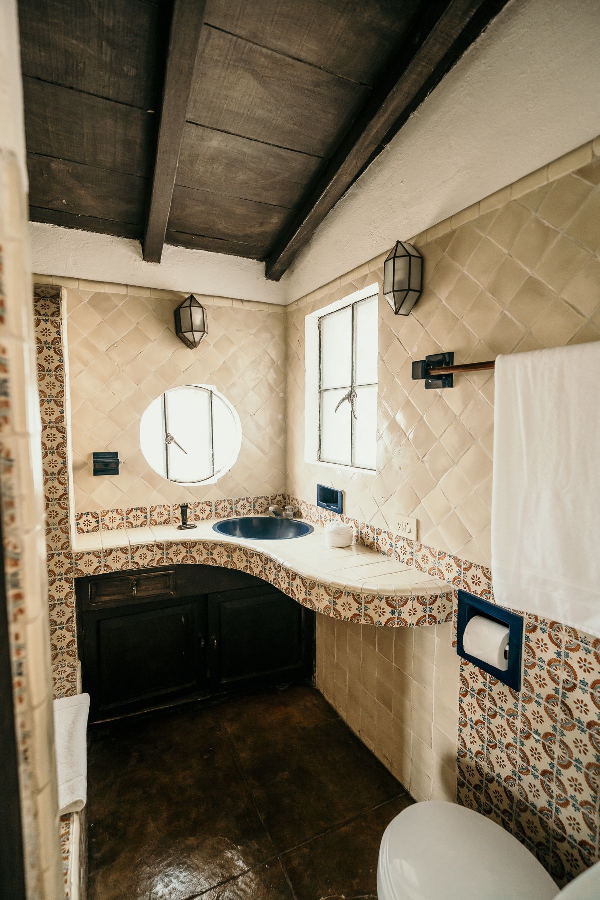 Baño con lavabo azul, tocador de madera oscura y azulejos estampados.