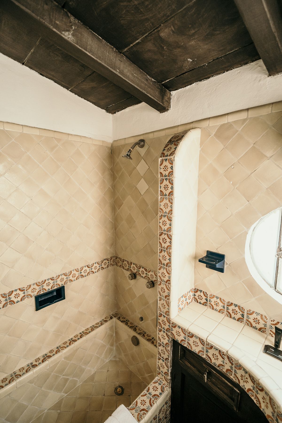 Baño con azulejos beige, molduras decorativas y vigas de madera en el techo.