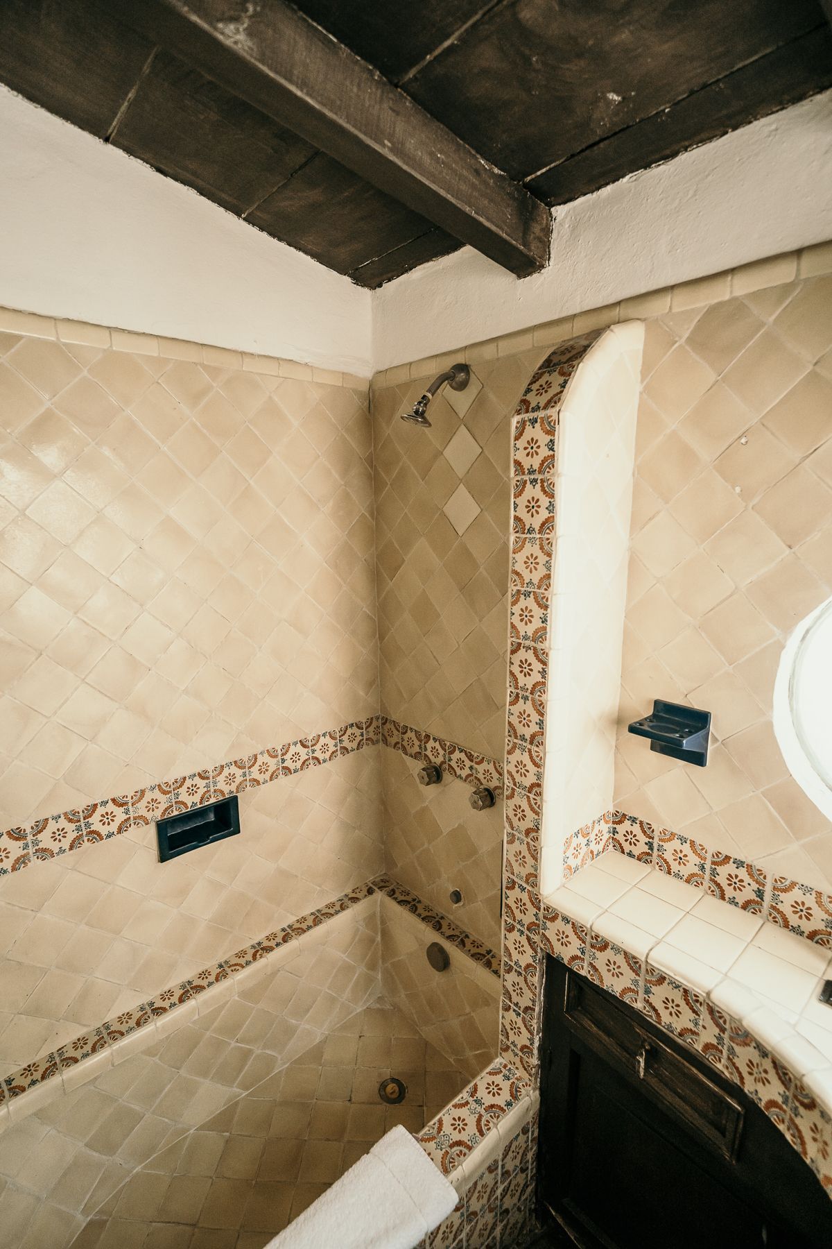 Baño con azulejos estampados en color beige, tocador de madera oscura y bañera.