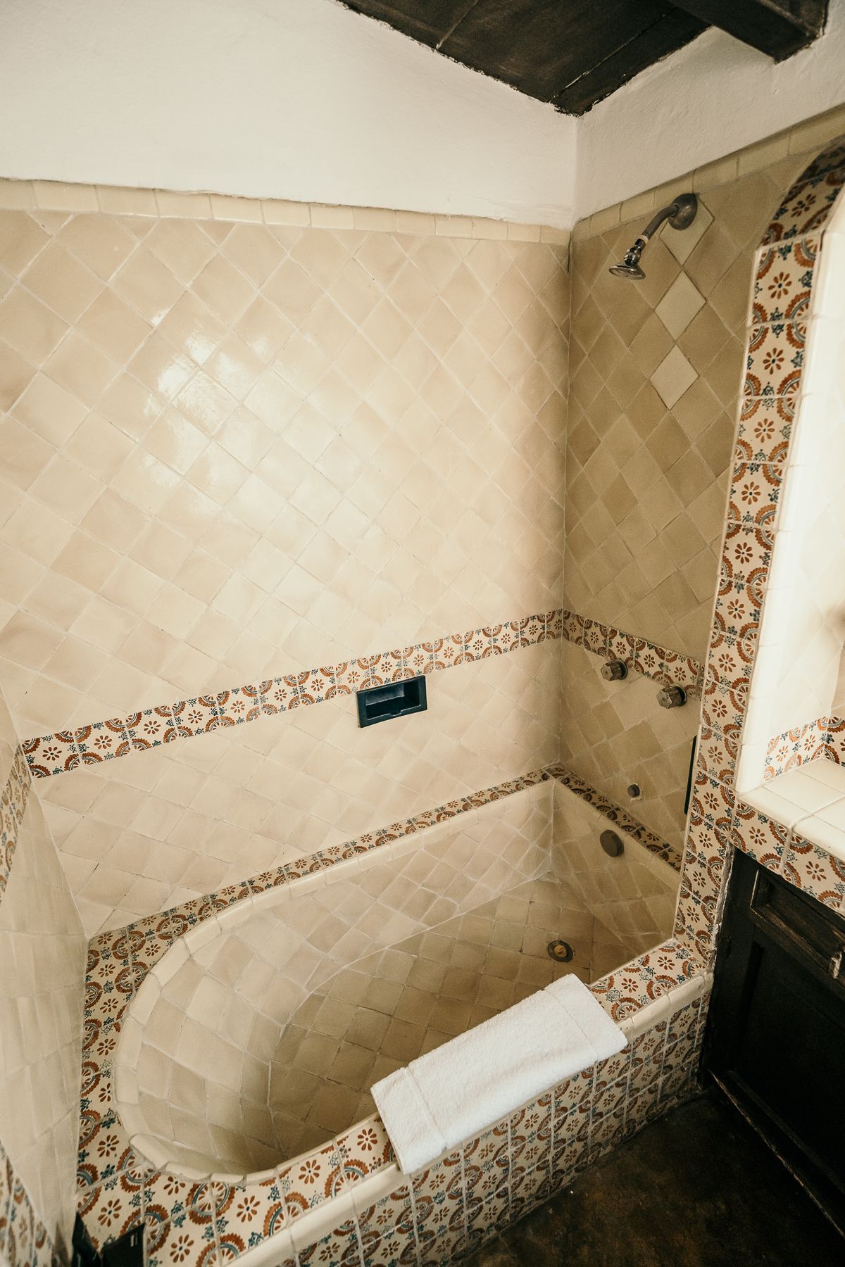 Baño alicatado con bañera ovalada, cenefas estampadas y toalla a un lado.