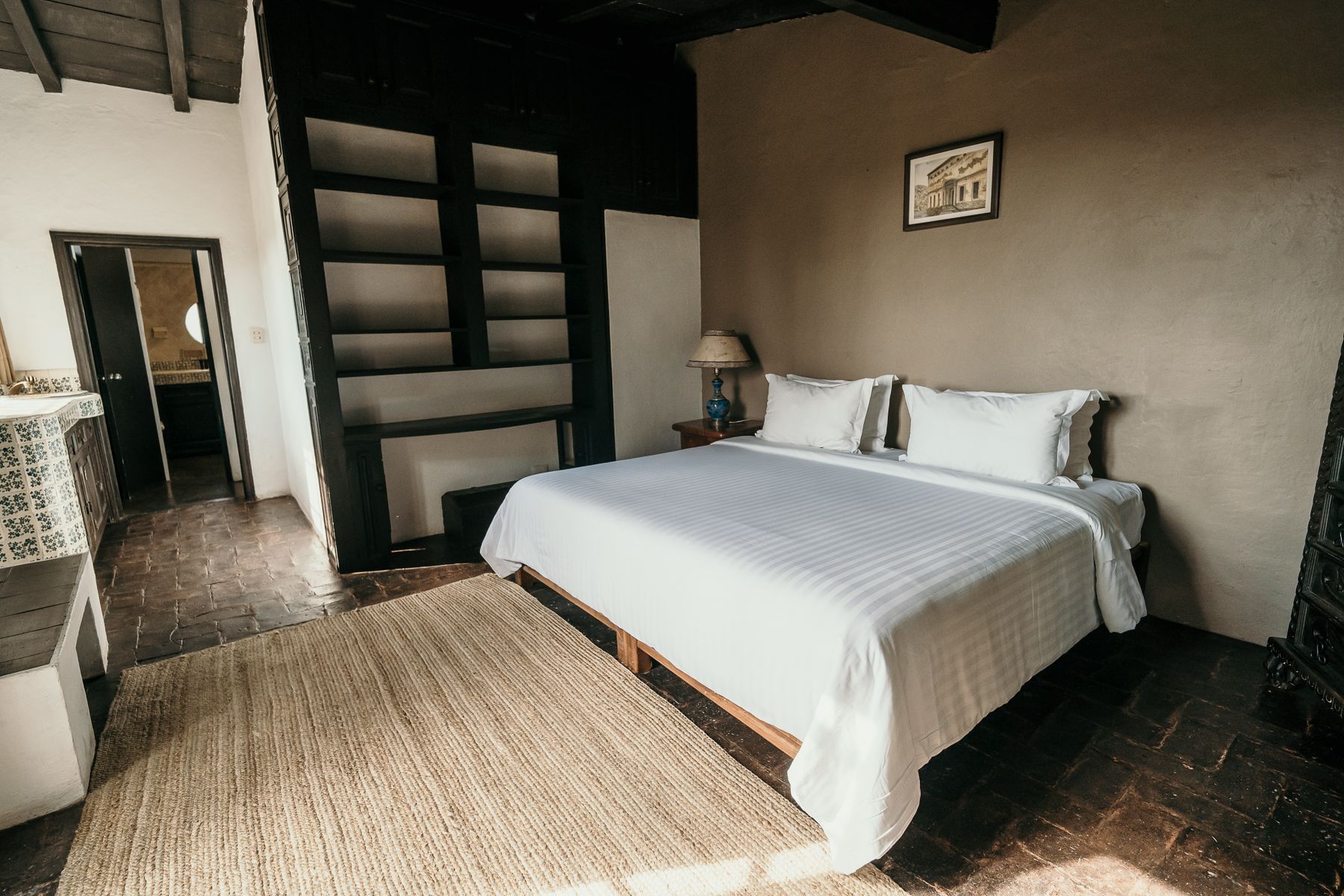 Dormitorio con cama, alfombra, estanterías empotradas y puerta abierta a un baño.